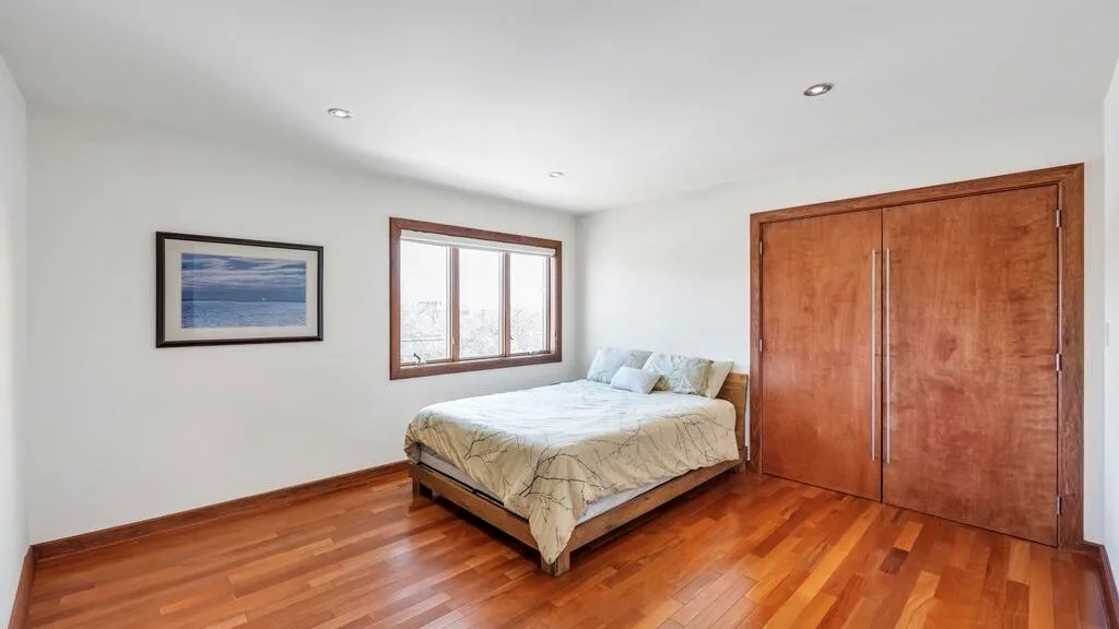 A bright bedroom with a bed beside a window and wooden closet doors.