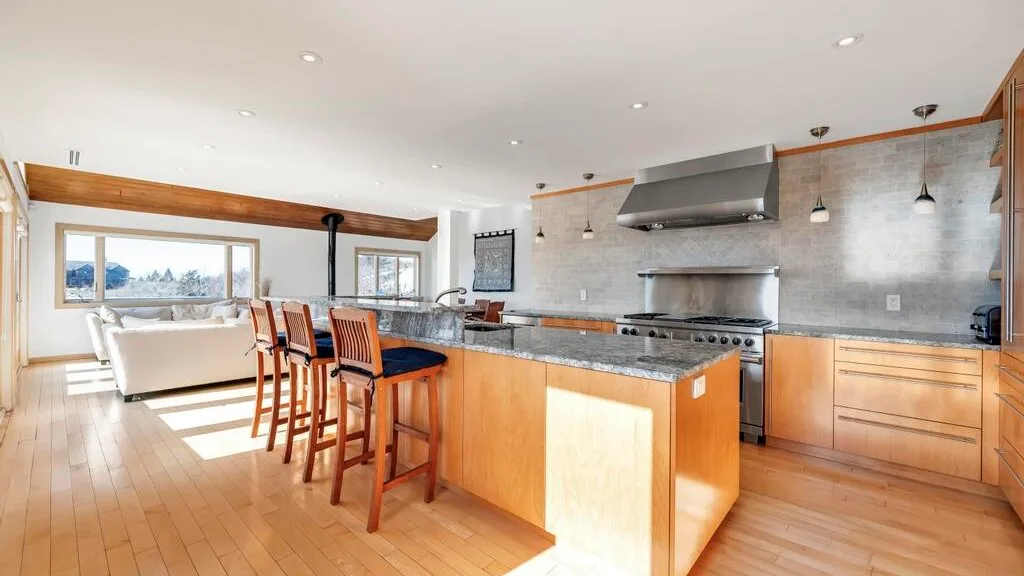 A bright open-plan kitchen with a central island and seating beside large windows.