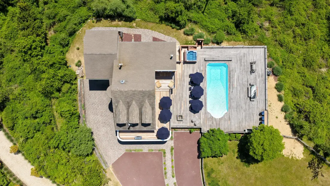 An aerial view of a house with a swimming pool amid green landscaping.