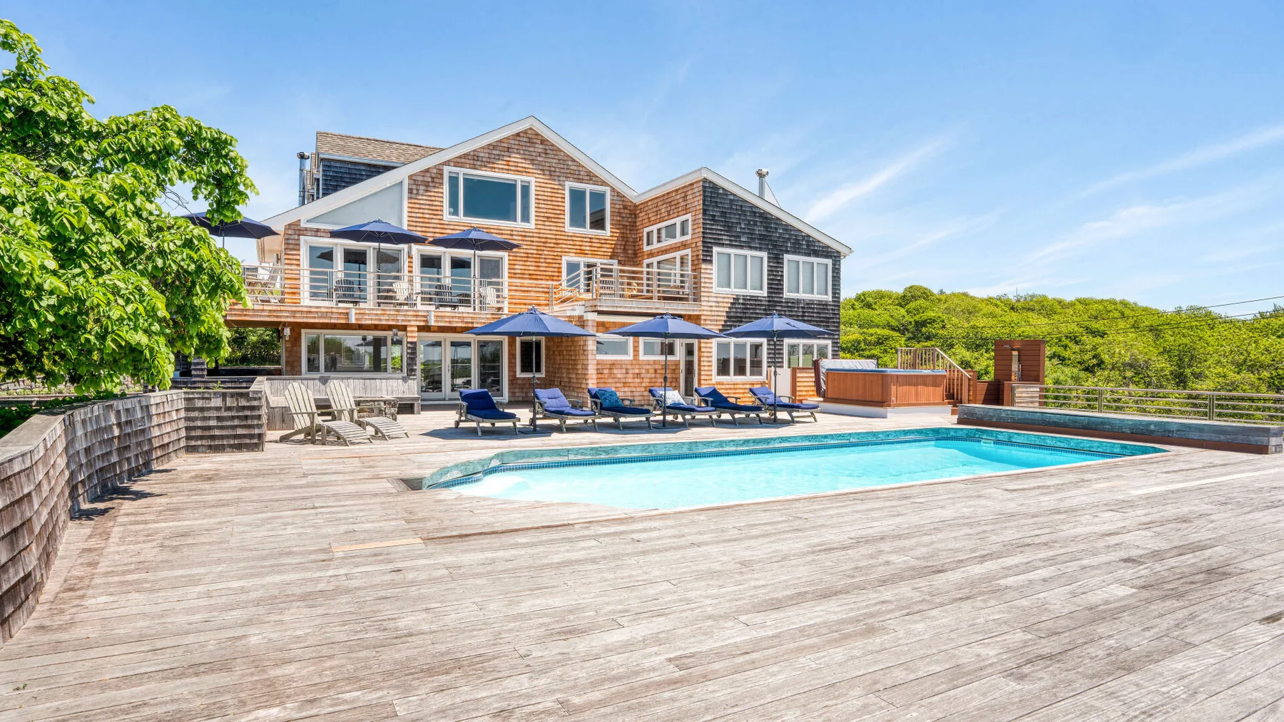 An outdoor swimming pool sits beside a spacious wooden deck and a large house.