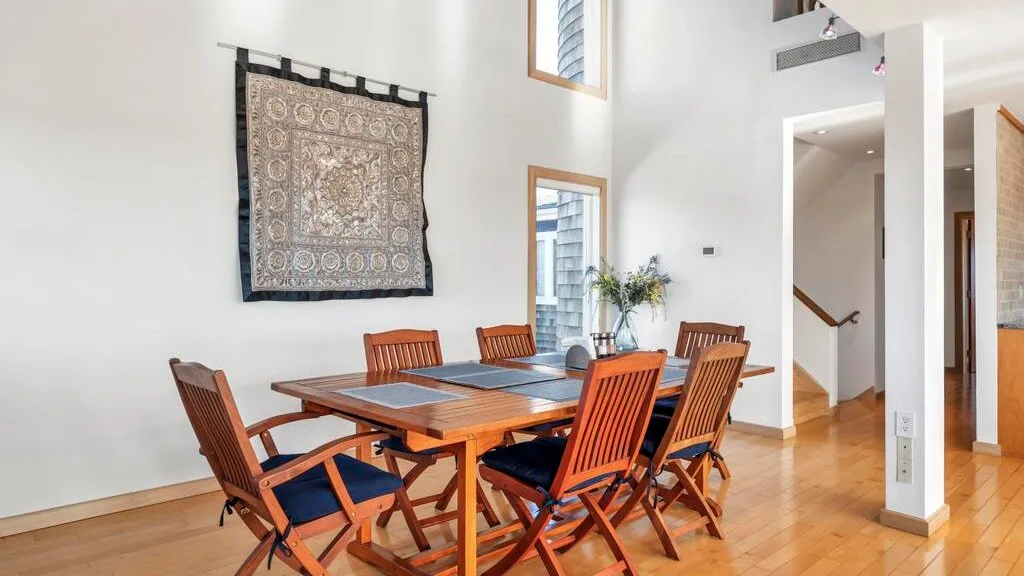 A dining area with a wooden table, matching chairs, and a decorative wall hanging.