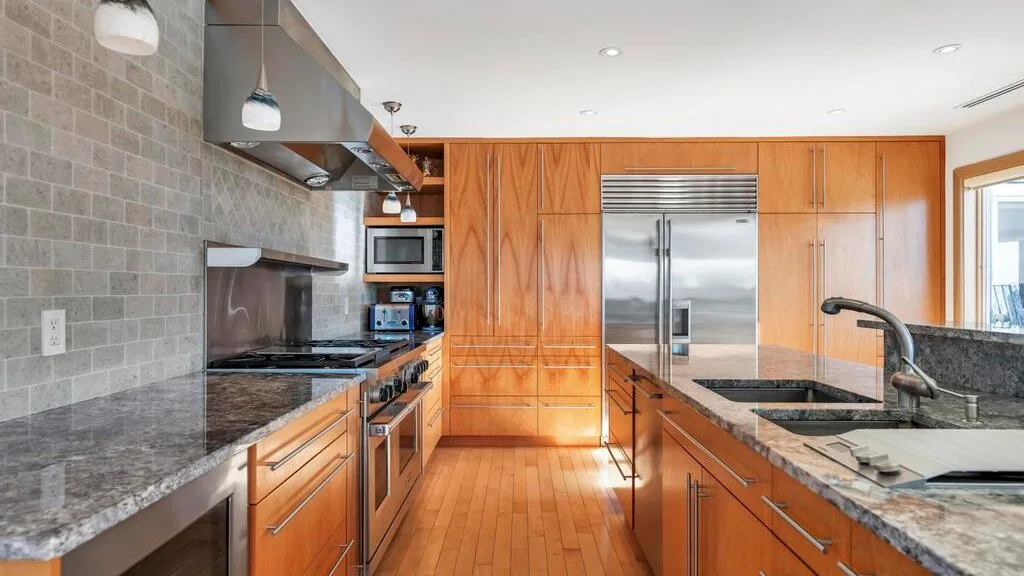 A kitchen with wooden cabinets, stone countertops, and stainless-steel appliances.
