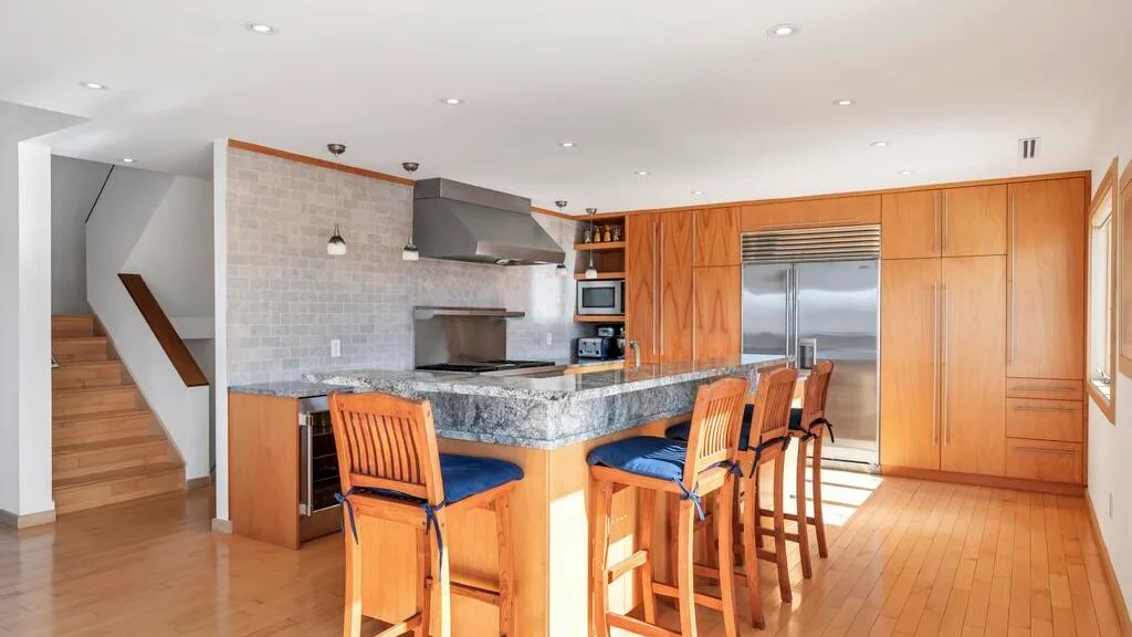 A bright kitchen with a central island and wooden seating.