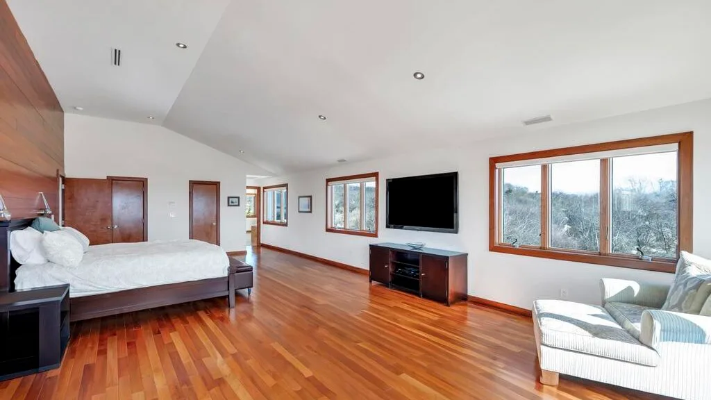 A spacious bedroom with a bed, television, and seating beside large windows.