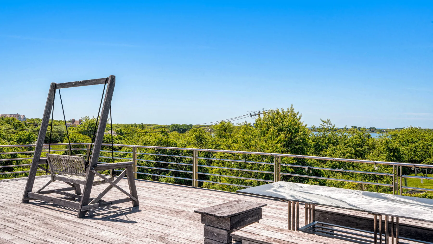A wooden deck with a suspended seat and a built-in rectangular feature overlooking greenery.