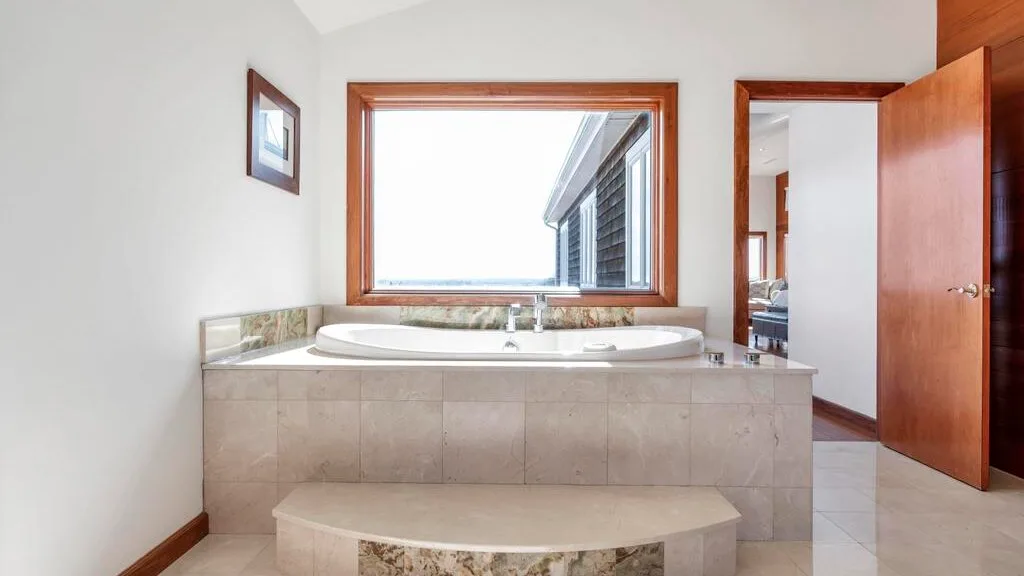 A bathroom features a built-in tub beneath a wide window.