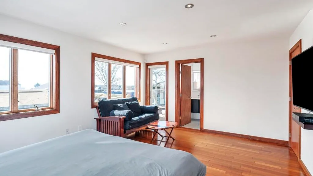 A bedroom with a bed, seating area, and several windows.