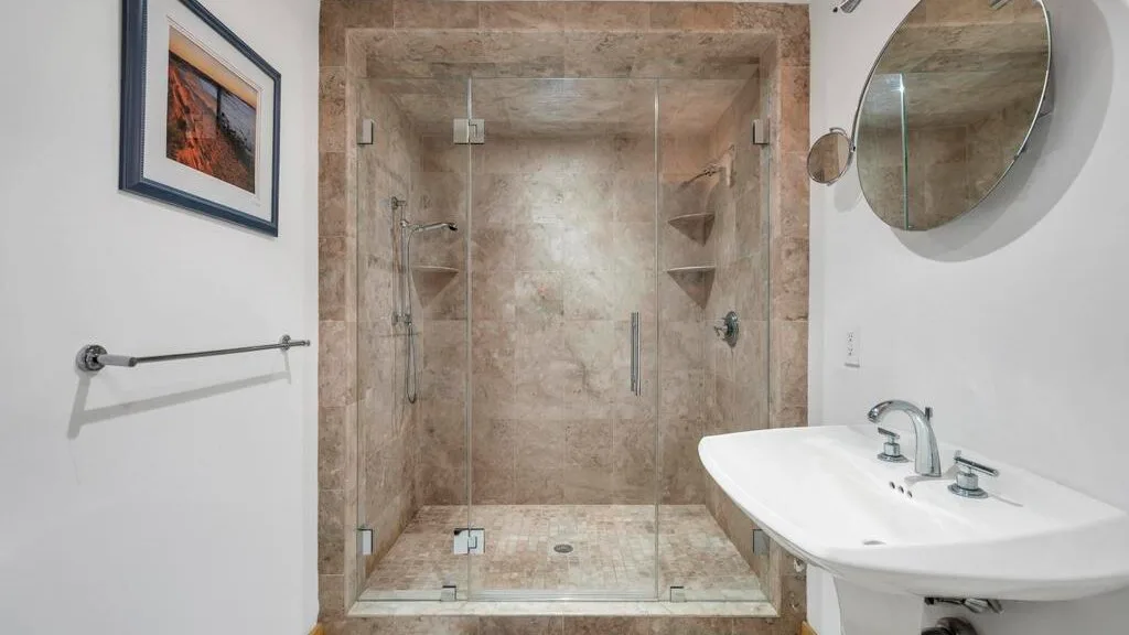 A bathroom with a glass shower, sink, and wall mirror.