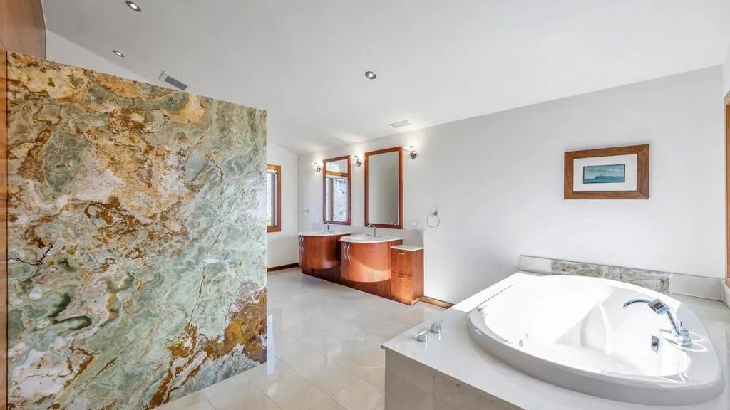 A bright bathroom features a large bathtub beside a decorative stone partition.