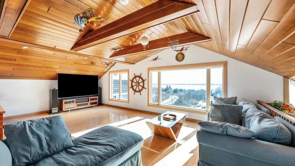 A bright living room with sloped wood ceilings, large windows, and seating.