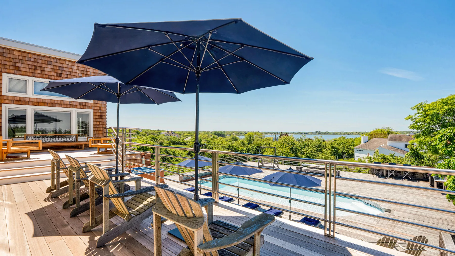 A sunny outdoor deck has wooden seating, large umbrellas, and a pool.