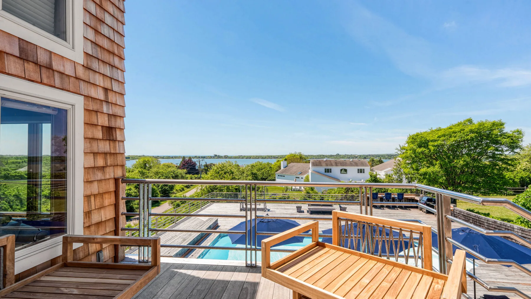 A sunny outdoor deck overlooks a swimming pool and a body of water.