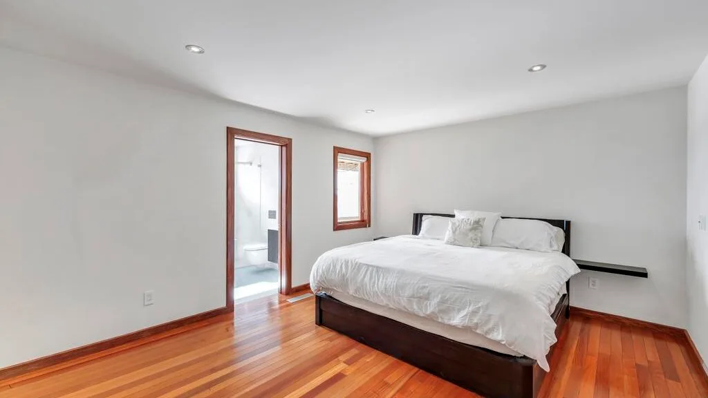 A bedroom with a bed, white bedding, and polished wood flooring.