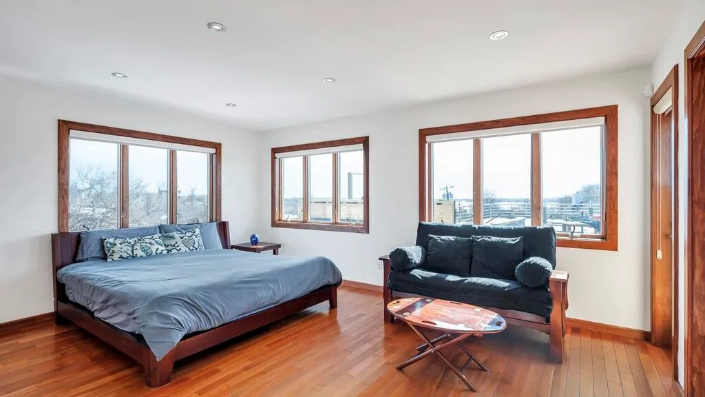 A bedroom with a bed and a seating area beside large windows.