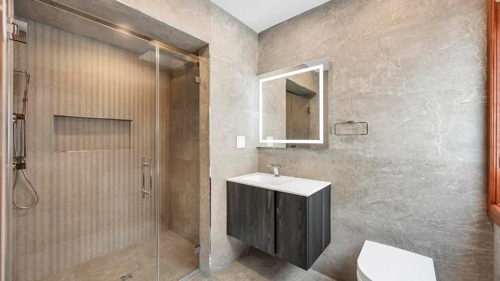 A bathroom with a glass shower, wall mirror, and dark vanity.