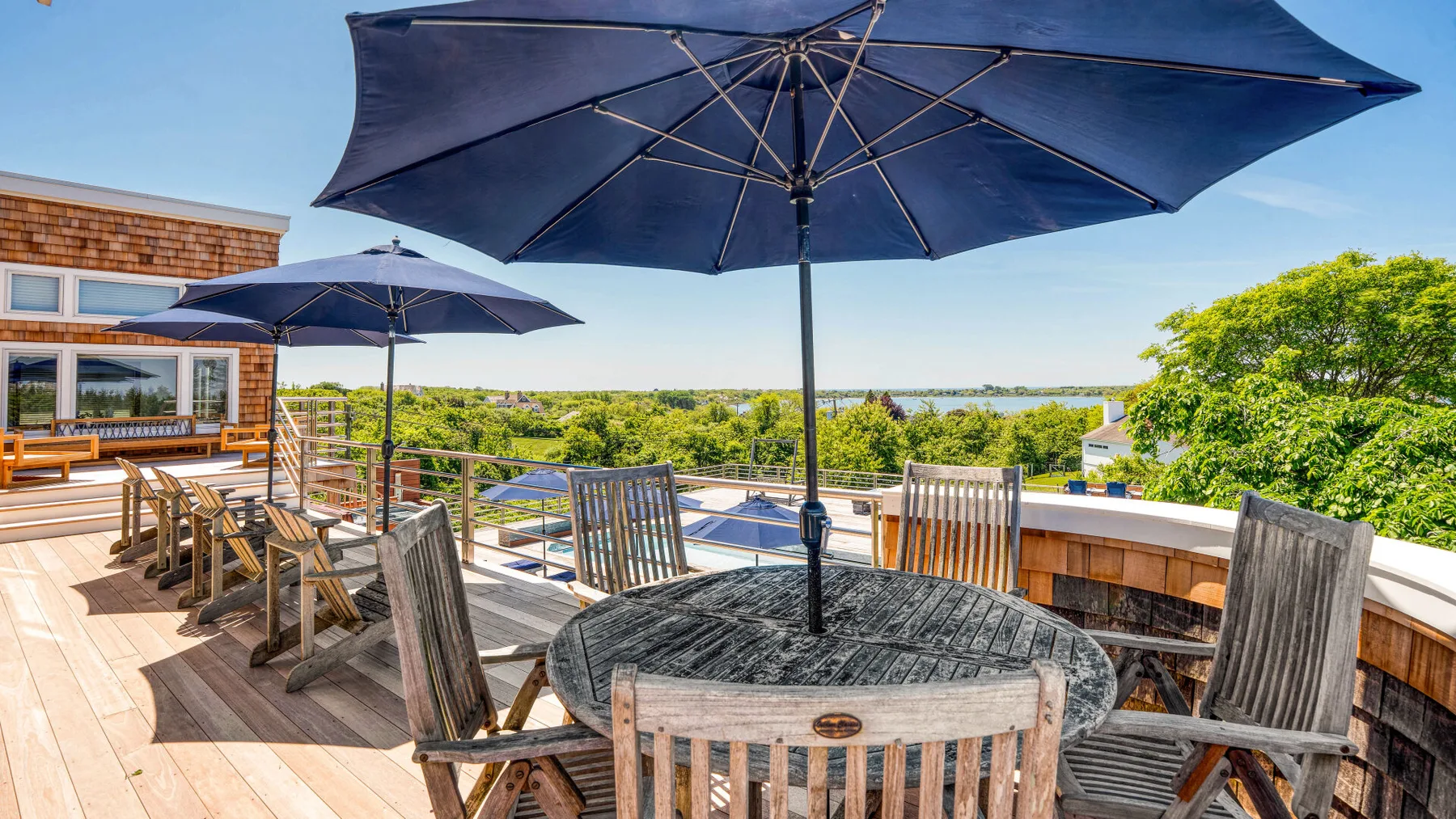 An outdoor dining terrace with wooden seating and large navy umbrellas overlooks the landscape.