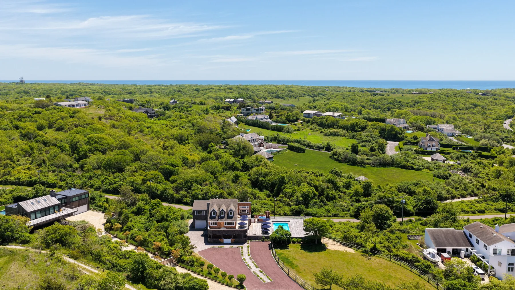 An aerial view of homes and a pool amid green vegetation near the coast.