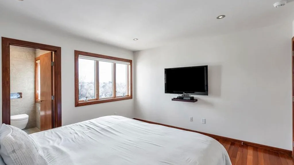 A bedroom with a bed, a window, and a wall-mounted television.