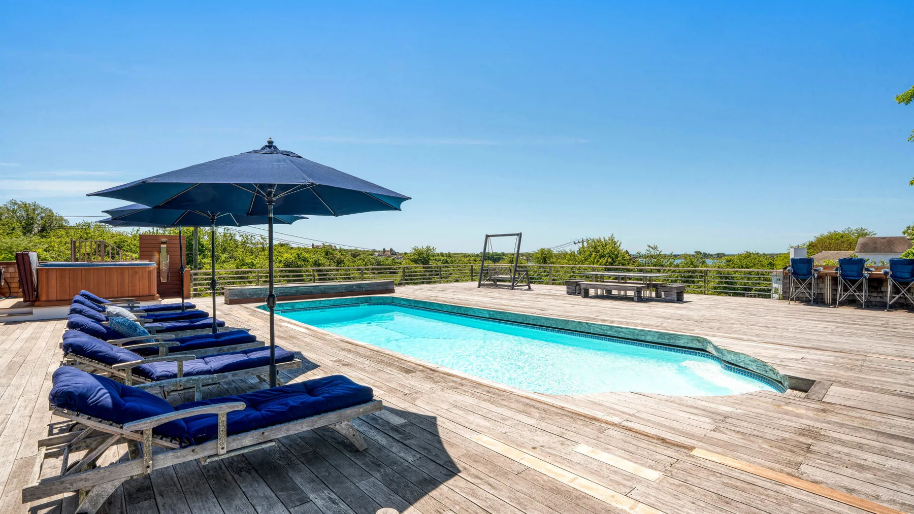 An outdoor swimming pool is surrounded by wooden decking and lounge seating.
