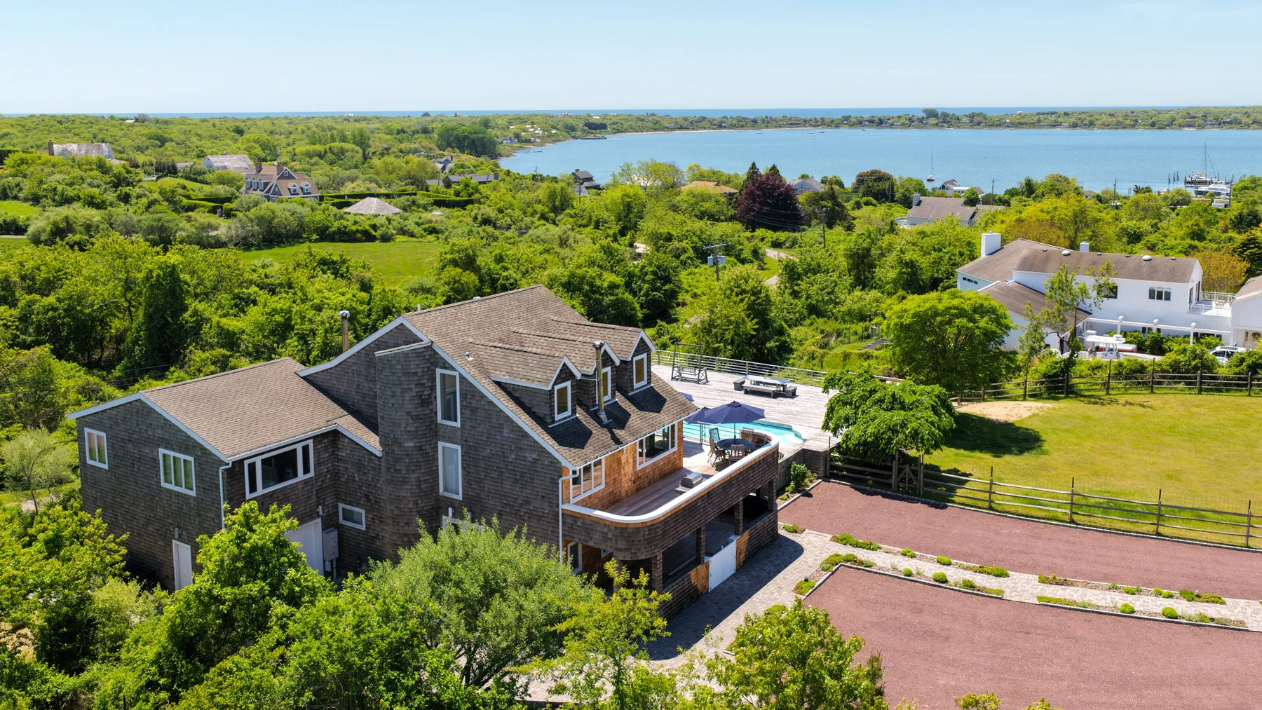 A large house stands amid green trees, with a paved area beside it.