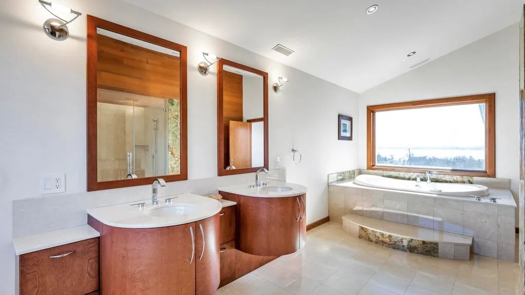 A bright bathroom with two sinks and a bathtub beneath a large window.