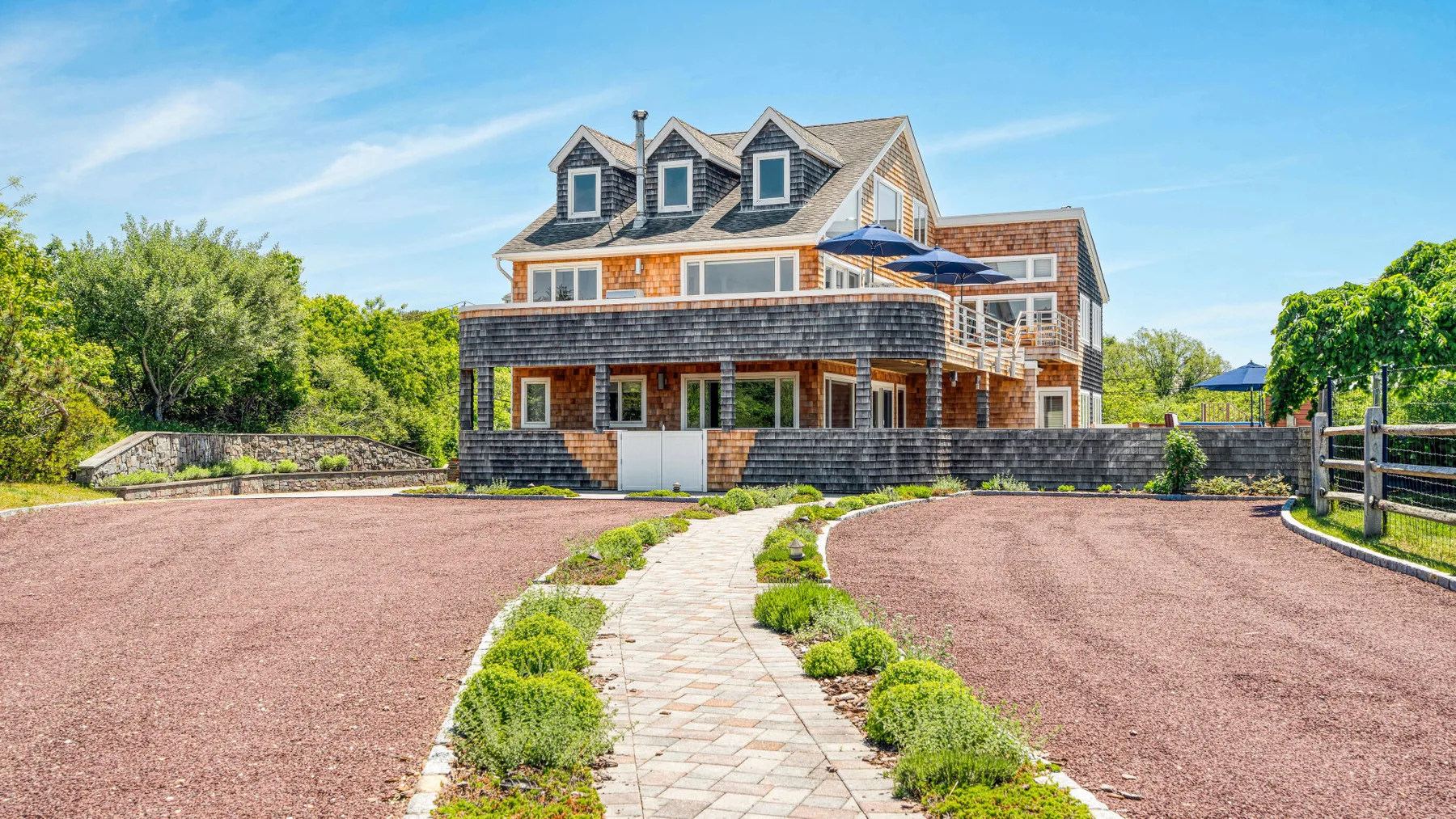 A large brick house stands beyond a paved walkway and landscaped driveway.