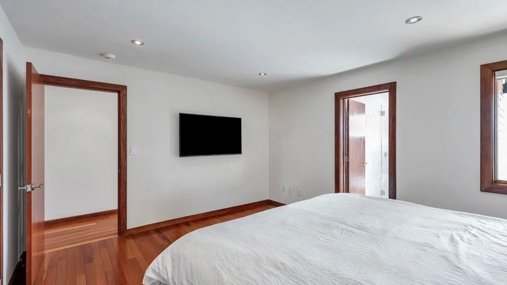 A bedroom with a bed, a wall-mounted television, and wood flooring.