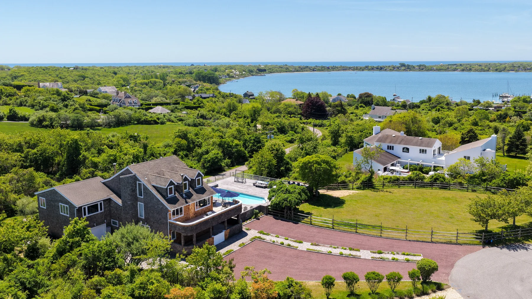 Aerial view of a large house beside a fenced lawn, with water visible in the distance.