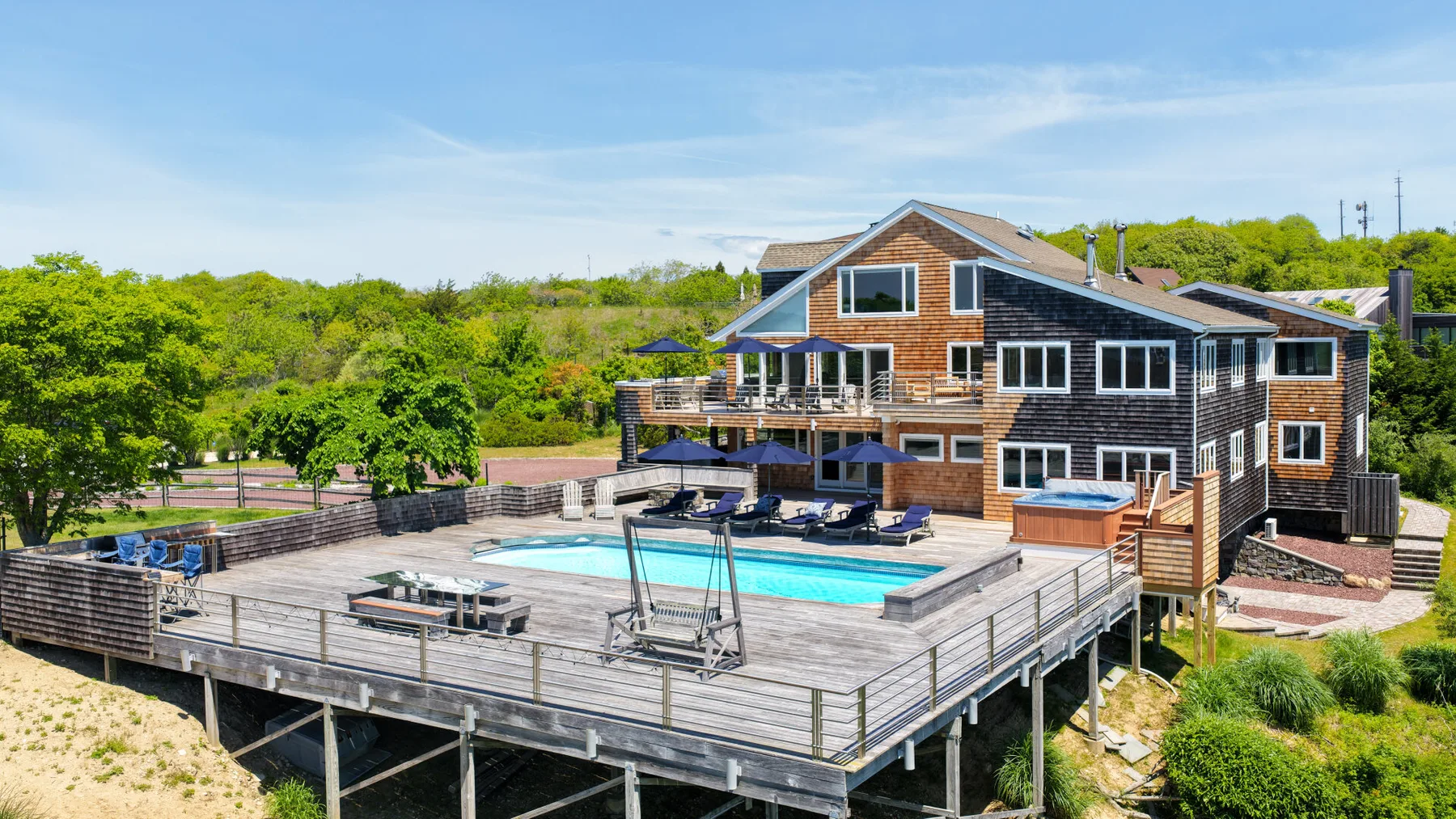 A large house overlooks a raised wooden deck with a swimming pool.