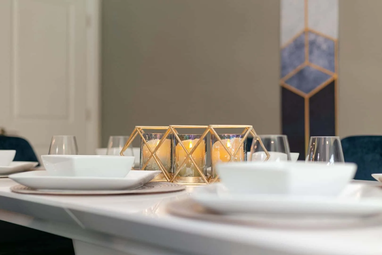 Una mesa está preparada con vajilla blanca y portavelas geométricos.