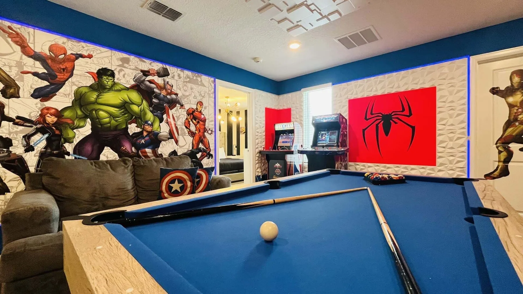 Una sala de juegos tiene una mesa de billar azul y murales coloridos de superhéroes.
