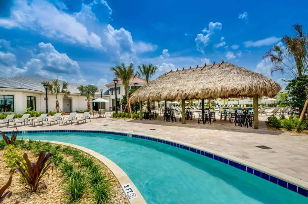 Una piscina al aire libre se curva junto a una zona de comedor con techo de paja.