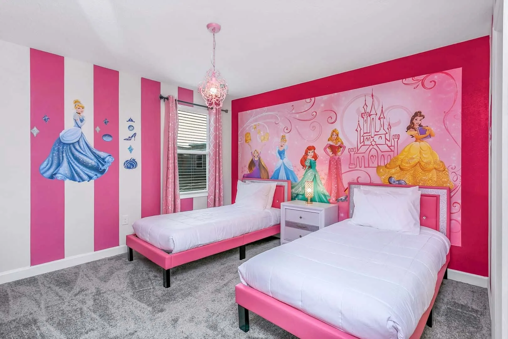 Un dormitorio de tonos rosados con dos camas y murales de princesas en las paredes.