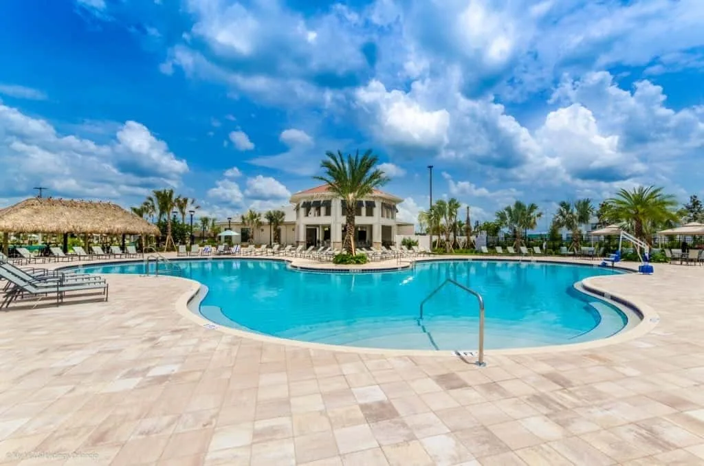 Una piscina al aire libre está junto a una terraza pavimentada y palmeras.