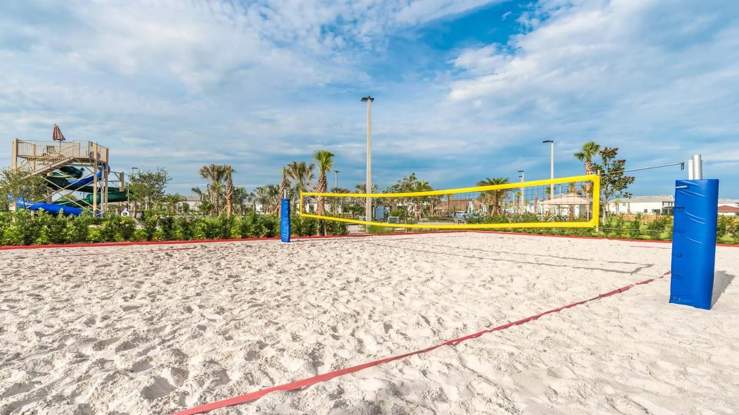 Una cancha de voleibol al aire libre con arena, red amarilla y postes azules.