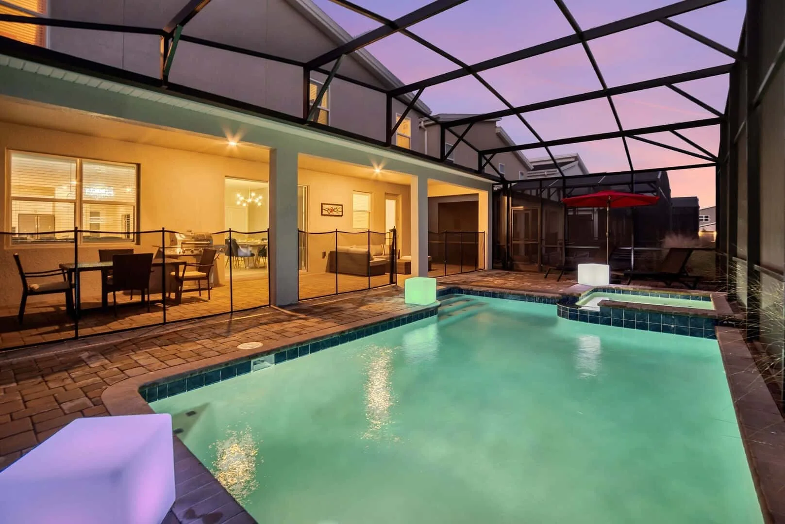 Una piscina iluminada está junto a un patio cubierto al anochecer.