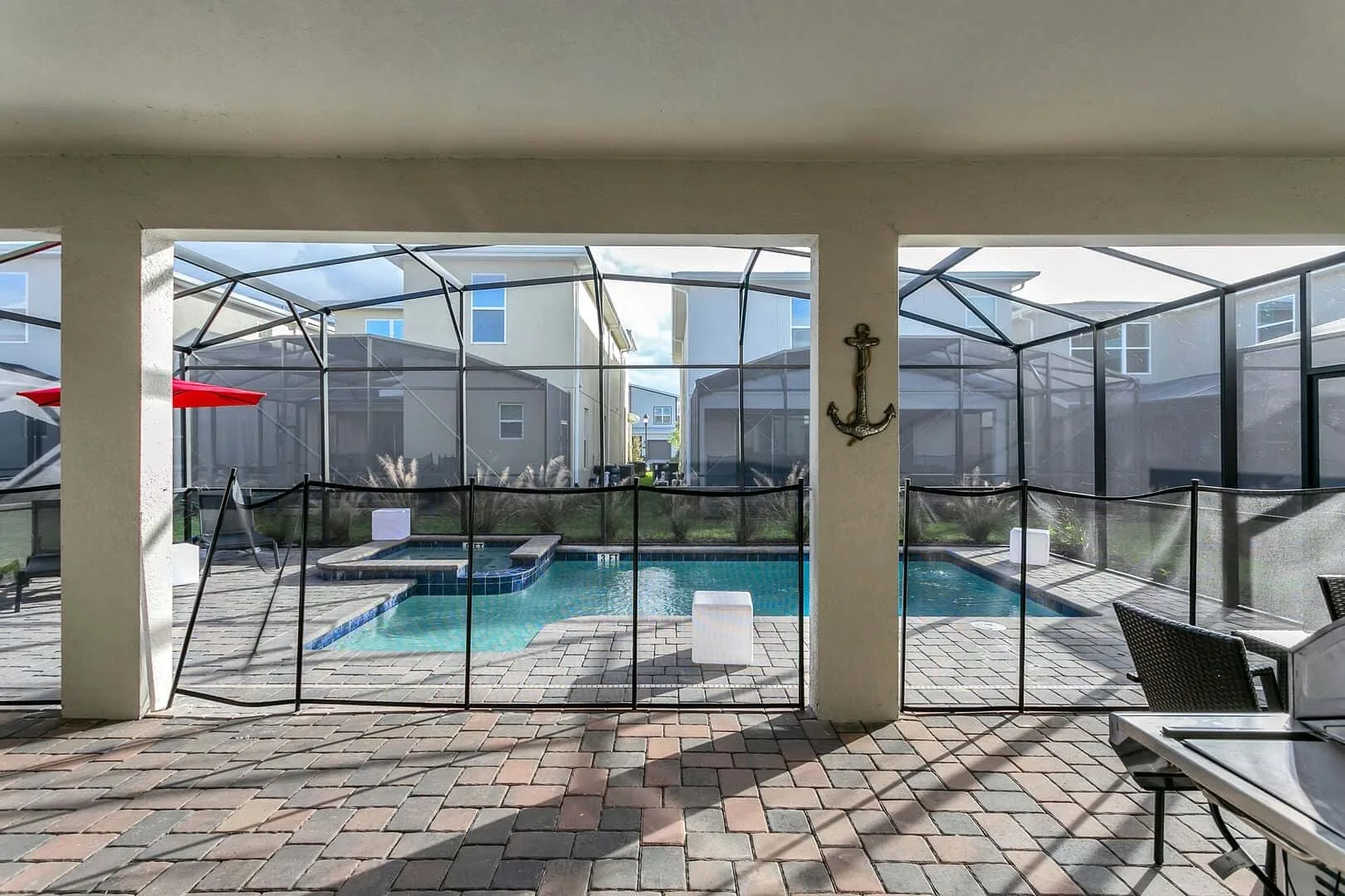 Una zona de piscina exterior con pantalla, asientos de patio y suelo pavimentado.