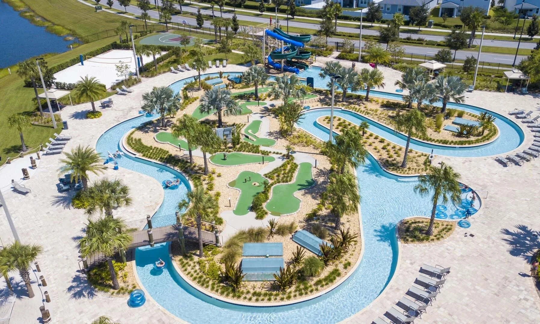Un parque acuático al aire libre cuenta con piscinas sinuosas, islas ajardinadas y un tobogán azul.