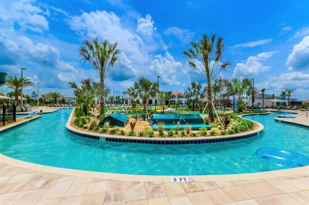 Una piscina turquesa al aire libre rodea una isla ajardinada con palmeras.