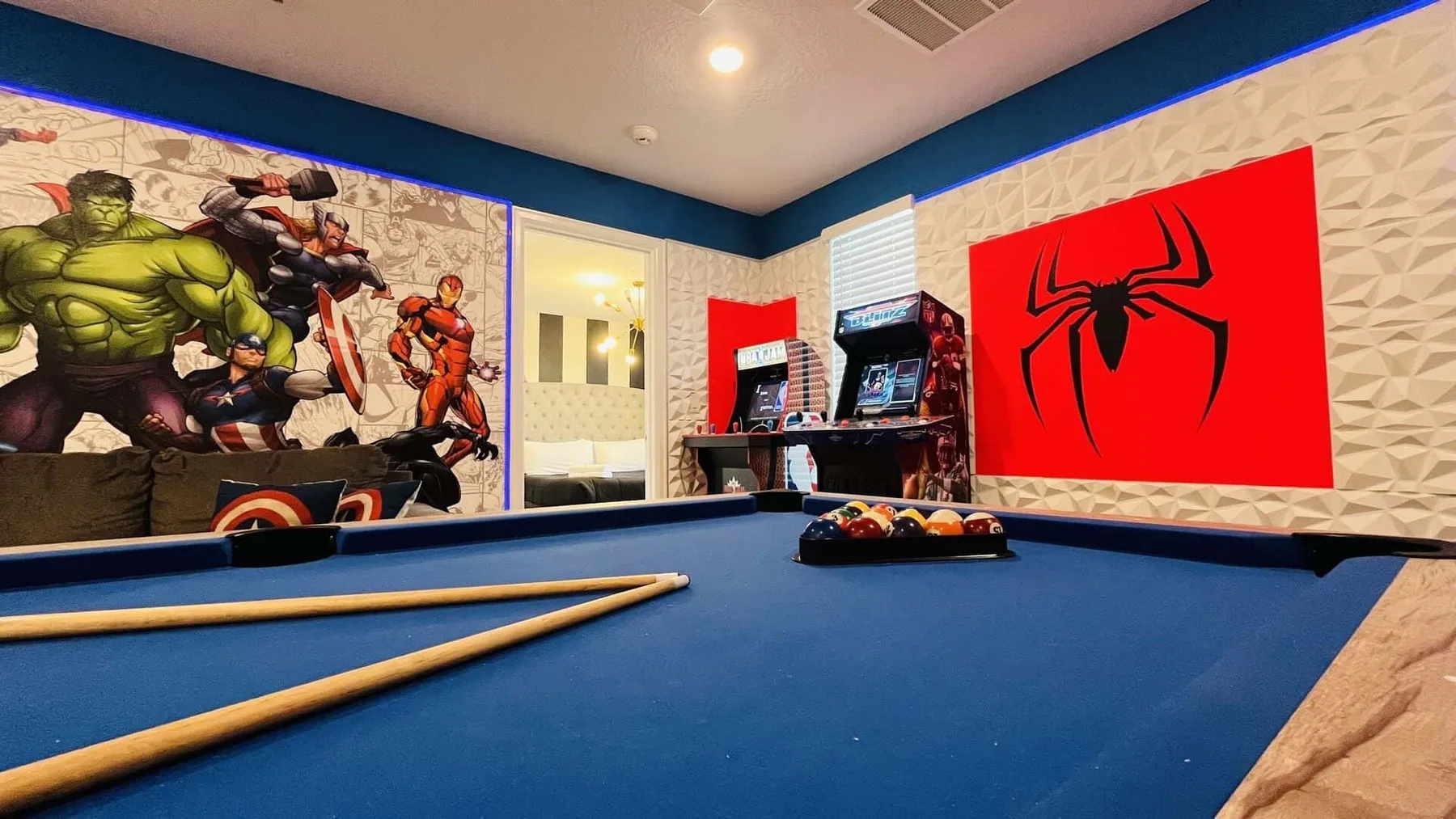Una sala de juegos tiene una mesa de billar azul y arte de superhéroes en las paredes.