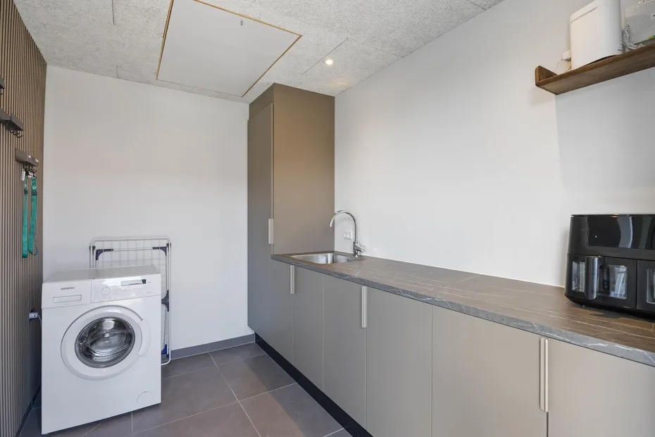 Un cuarto de lavandería con una lavadora junto a una encimera larga y un fregadero.