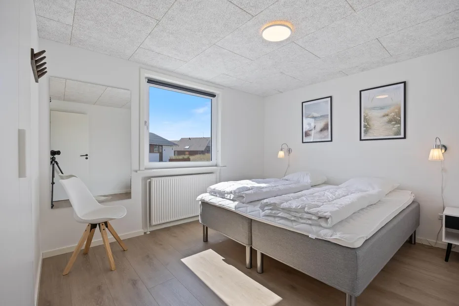 Un dormitorio luminoso con dos camas, una ventana y cuadros en la pared.