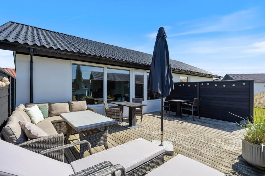 Un patio exterior con asientos, una mesa y una sombrilla cerrada.