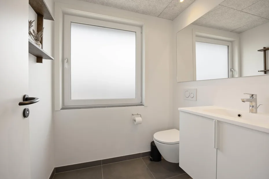 Un baño moderno con inodoro suspendido, mueble de lavabo y una ventana grande.