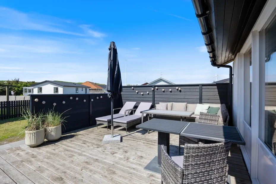 Una terraza exterior con asientos, una mesa y una sombrilla cerrada.
