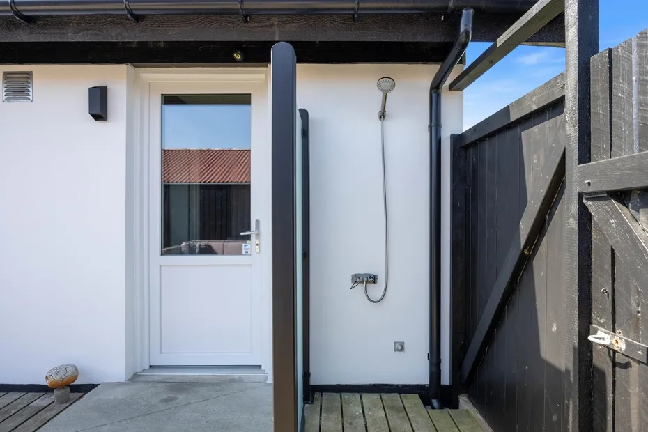 Una ducha exterior junto a una puerta blanca, rodeada por una cerca de madera oscura.