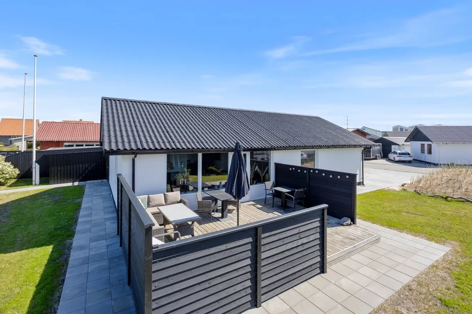 Una casa moderna tiene un patio pavimentado con asientos al aire libre y una sombrilla cerrada.
