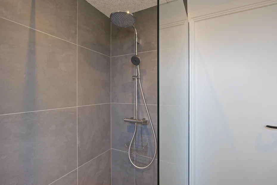 Una ducha con azulejos, cabezal fijo y rociador de mano.