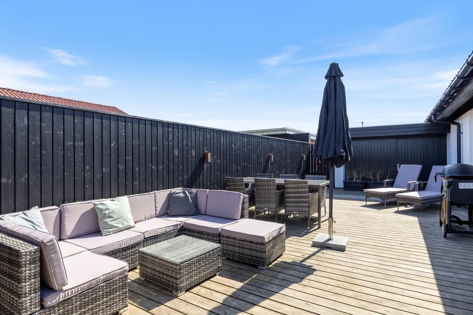 Una terraza exterior con una zona de estar, una mesa de comedor y una sombrilla cerrada.