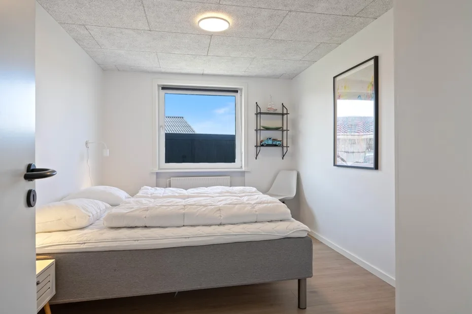 Un dormitorio con una cama bajo una ventana y una pequeña repisa en la pared.